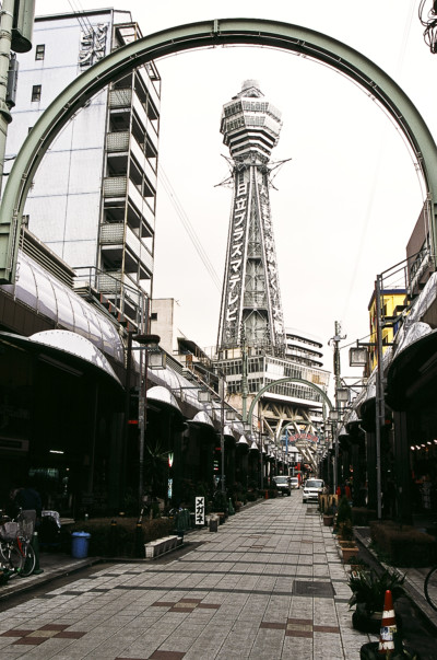 Tsutenkaku (通天閣, Tsūtenkaku), lit. "Tower Reaching Heaven", owned by Tsutenkaku Kanko Co., Ltd. is a well-known landmark of Osaka, Japan and advertises Hitachi, Ltd. The current tower is actually the second to occupy the site. The original tower, patterned after the Eiffel Tower, was built in 1912, and was connected to the adjacent amusement park, Luna Park, by an aerial cable car. It quickly became one of the most popular locations in the city, drawing visitors from all over the area. The Japanese government dismantled the tower in 1943, believing that it would serve as a reference point for American bombing raids on Osaka: the iron in the tower was melted down and used for war material. After the war citizens lobbied to rebuild the beloved tower. A private company, the Tsutenkaku Kanko Co. Ltd. was established and on October 28, 1956, the second-generation tower was opened. On the fifth floor observation deck is enshrined Billiken, the God of Happiness or "things as they ought to be."Billiken, a popular American charm doll that came to Japan in about 1910, was enshrined within Luna Park when it opened. When the park was closed in 1923, the wooden statue of Billiken went missing. As a part of an effort to revive the tower, a copy of Billiken was made from an old photograph and placed inside the tower in 1979. The statue of Billiken has became closely associated with the tower and is a popular symbol of good luck. Each year thousands of visitors place a coin in his donation box and rub the soles of his feet to make their wishes come true. (Source: http://en.wikipedia.org/wiki/Tsutenkaku)