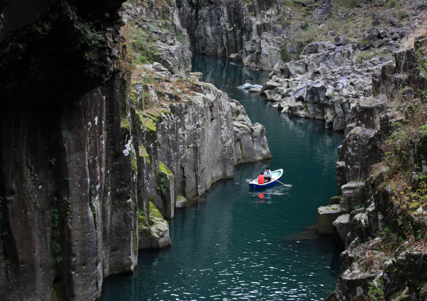 Two people in a rowboat, on the water of a narrow gorge