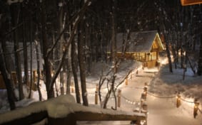 Snow-covered path at Ningle Terrace - The line of illuminated log cabins gives this place a cozy atmosphere