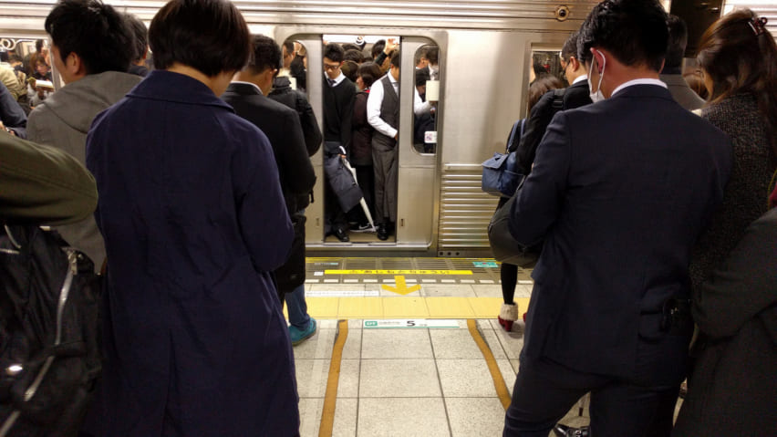 Commuters waiting in lines on the platform as the doors to a packed train close